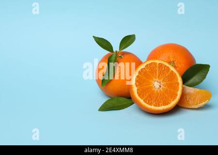 Reife Mandarinen mit Blättern und einer halbierten Frucht auf blauem Hintergrund mit Platz für Text, ein frisches Zitrus-Banner Stockfoto