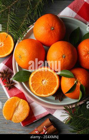 Teller mit Mandarinen und Tannenwedeln sowie einer rot karierten Serviette auf einem dunklen Tisch, ein gemütliches Weihnachtsstilleben Stockfoto