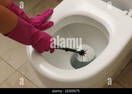 Frau in Gummi rosa Handschuhe reinigt Toilettenschüssel mit Pinsel Stockfoto