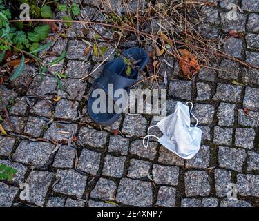 Corona Still Life - verlassene oder verlorene Gesichtsmaske und Kleine Gummisandale auf einem gepflasterten Bürgersteig in Mitte, Berlin Stockfoto