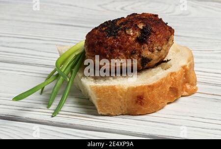 Gebratenes Fleischschnitzel mit grünen Zwiebeln auf einem Stück Weißbrot Stockfoto