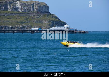 Eine Gruppe von Touristen auf einer Schnellbootfahrt vor Llandudno's North Shore mit dem Pier und Great Orme Beyond. Stockfoto