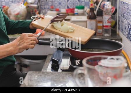 Ältere Frau, die Zwiebeln in die Bratpfanne legt. Stockfoto