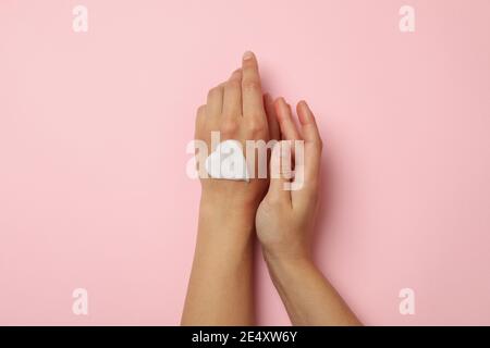 Weibliche Hände mit Herz aus kosmetischer Creme auf rosa Hintergrund Stockfoto