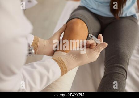 Nahaufnahme eines Arztes, der einem Patienten mit einem verletzten Bein eine Injektion in das Knie verabreicht. Stockfoto