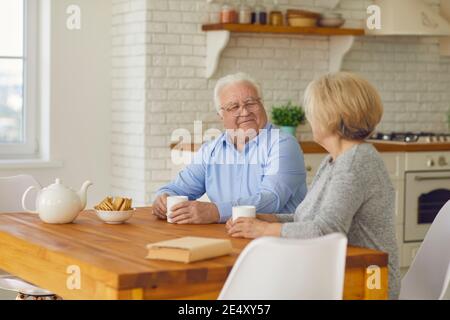 Glückliches Seniorenpaar sitzt am Küchentisch, trinkt Tee und genießt ruhige Unterhaltung Stockfoto
