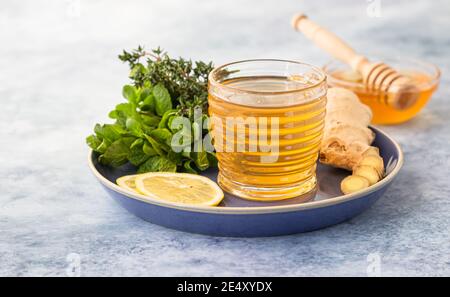 Eine Tasse frischen Kräutertee mit Thymian, Minze, Ingwer, Zitrone und Honig auf blauem Betongrund. Selektiver Fokus. Stockfoto