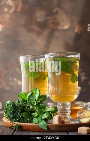 Warme Kräutergetränk Infusion in Gläsern für kalte Tage. Zwei Tassen Ingwertee mit Minze, Thymian und Honig auf einem Holztisch. Selektiver Fokus. Stockfoto