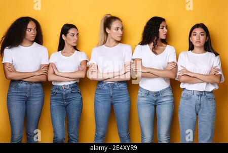 Unzufriedene Multirassische Damen Mit Blick Auf Asiatische Weibliche Stehend, Gelber Hintergrund Stockfoto