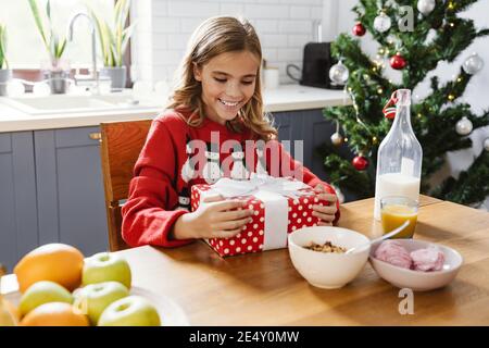 Glücklich kaukasischen Mädchen Eröffnung Weihnachtsgeschenk beim Frühstück Wohnküche Stockfoto