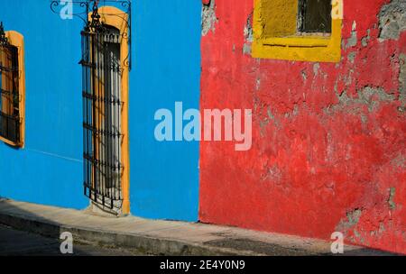Alte traditionelle Hausfassade mit einer bunten Stuckwand und Fenstern mit handgefertigten Eisengittern in Atlixco, Puebla Mexiko. Stockfoto
