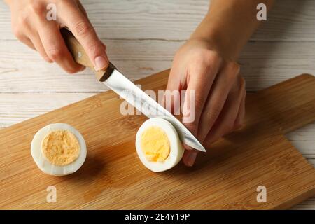 Frau schneidet gekochtes Ei an Bord auf weißem Holzhintergrund Stockfoto