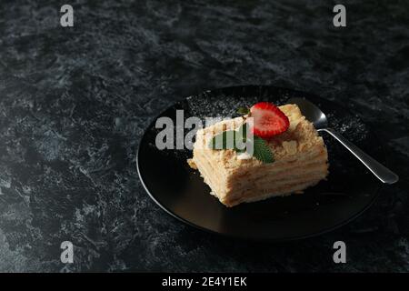 Teller mit Stück Napoleonkuchen mit Erdbeere auf schwarz Rauchige Hintergrundfarbe Stockfoto