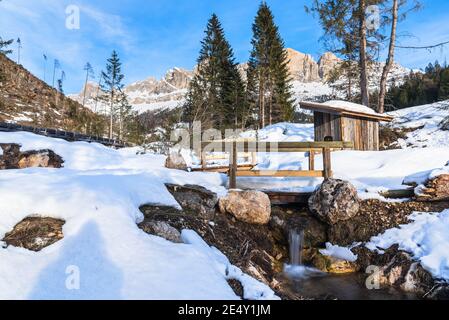 Kleine Holzbrücke über einen Bach in einem majestätischen Schnee Berglandschaft an einem sonnigen Wintertag Stockfoto