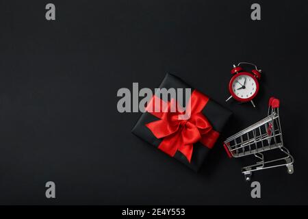 Wecker, Geschenkkiste und Einkaufswagen in einer dunklen Black-Friday-Szene, ein Last-Minute-Angebotskonzept mit Platz für Text Stockfoto