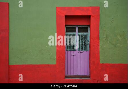 Koloniale Hausfassade mit einer rot getrimmten olivgrünen Stuckwand und einer handgefertigten eisernen rosafarbenen Tür in Atlixco, Puebla Mexiko. Stockfoto