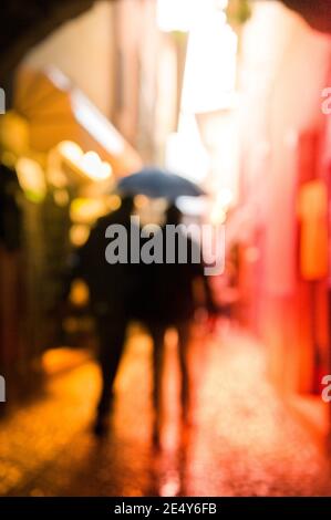 Menschen, die im Regen entlang einer engen Straße in Malcesine, am Ostufer des Gardasees in der Region Venetien in Italien. Stockfoto