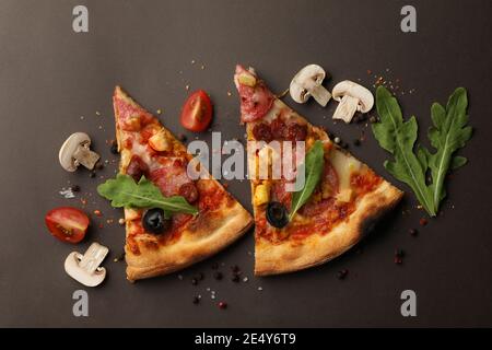 Pizzascheiben und Zutaten auf dunklem Hintergrund Stockfoto