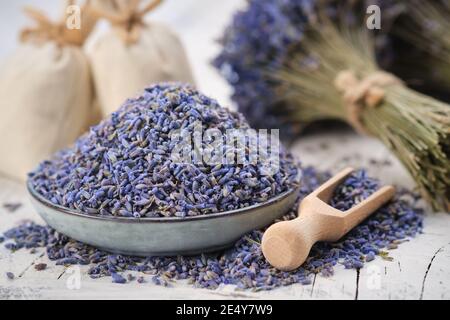 Blauer Teller mit getrocknetem Lavendel. Holzlöffel von trockenen Lavendelblüten. Lavendelbukett und Beutel auf dem Hintergrund. Stockfoto