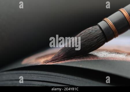 Nahaufnahme eines künstlerischen Pinsels für Aquarellmalerei. Malen mit einem Pinsel in einem Skizzenbuch auf schwarzem Papierbogen. Stockfoto