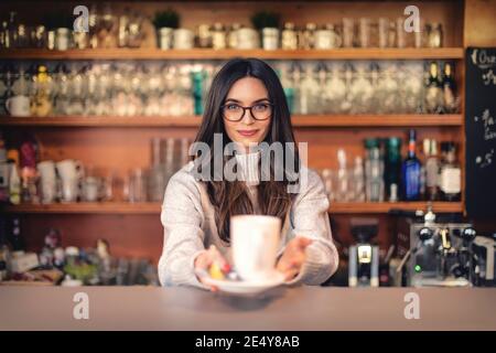 Aufnahme einer lächelnden Kellnerin, die hinter dem Tresen stand und eine Tasse Tee in der Hand hielt. Stockfoto