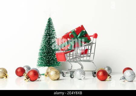 Einkaufswagen mit einer Weihnachtsbox und dekorativen Accessoires auf weißem Hintergrund, symbolisiert Weihnachtseinkäufe und die Verkaufssaison Stockfoto