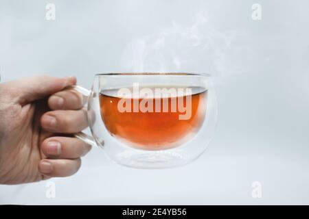 Hand des Mannes hält eine transparente Tasse mit Tee. Isoliert auf weißem Hintergrund. Alpha Stockfoto