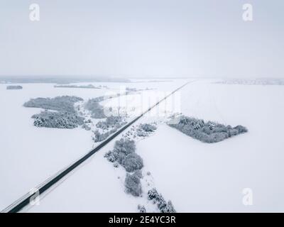 Drohne Blick auf die Straße, schneebedeckte Felder und Bäume an einem winterlichen bewölkten Tag. Wunderschöne Winterlandschaft Stockfoto