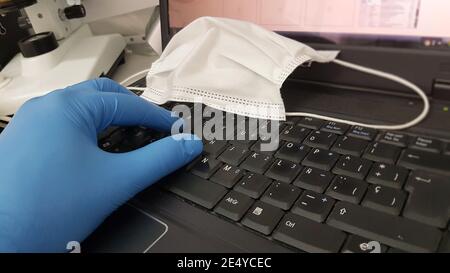 Ein Forscher oder Wissenschaftler forscht am Computer mit Eine medizinische Gesichtsmaske auf der Tastatur Stockfoto