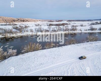 Wunderschöne Winterlandschaft, Sonnenuntergang über dem Dnjepr River, Blick von einer Drohne. Das Auto fährt auf einer schneebedeckten Straße entlang des Flusses. Stockfoto