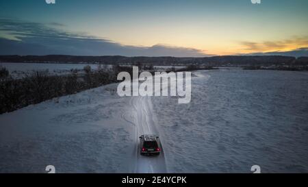 Wunderschöne Winterlandschaft, Sonnenuntergang über dem Dnjepr River, Blick von einer Drohne. Das Auto fährt auf einer schneebedeckten Straße entlang des Flusses. Stockfoto