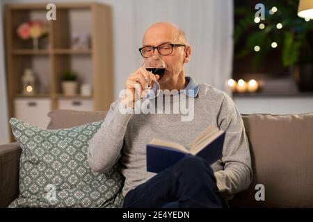 Älterer Mann mit Buch trinkt Rotwein zu Hause Stockfoto