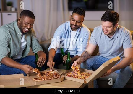 Glückliche männliche Freunde mit Bier essen Pizza zu Hause Stockfoto