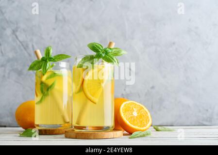 Limonade mit Orange und Basilikum, kaltes Erfrischungsgetränk in Gläsern auf grauem Hintergrund Stockfoto