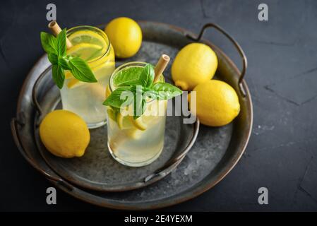 Limonade mit Zitrone und Basilikum, kaltes Erfrischungsgetränk in Gläsern auf schwarzem Hintergrund Stockfoto