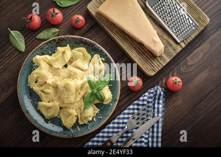 Italienische Ravioli gefüllt mit Ricotta-Käse und Spinat beträufelt mit geriebenem Parmesan auf einem Teller auf einem hölzernen Hintergrund, Draufsicht Stockfoto