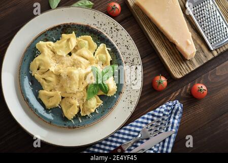 Italienische Ravioli gefüllt mit Ricotta-Käse und Spinat beträufelt mit geriebenem Parmesan auf einem Teller auf einem hölzernen Hintergrund, Draufsicht Stockfoto