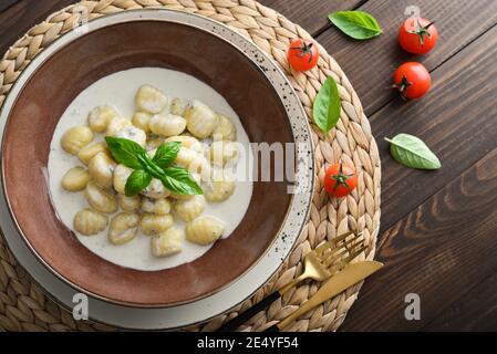 Hausgemachte Gnocchi mit cremiger Gorgonzola-Sauce in brauner Platte auf Holzhintergrund, Draufsicht Stockfoto