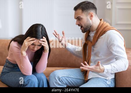 Aggressiver Mann Schrie Unglückliche Frau Auf Sofa Drinnen Sitzen Stockfoto