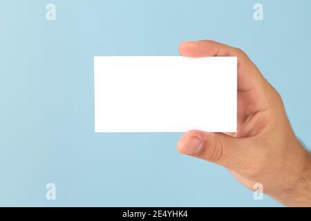 Männliche Hand mit leerer Visitenkarte auf hellblauem Hintergrund. Modell für dein Design Stockfoto