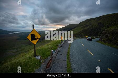 Auto fährt durch die Spitze der Connor Pass Straße auf der Dingle Halbinsel, Grafschaft Kerry, Irland, enge kurvenreiche Straße und fallenden Felsen Zeichen Stockfoto