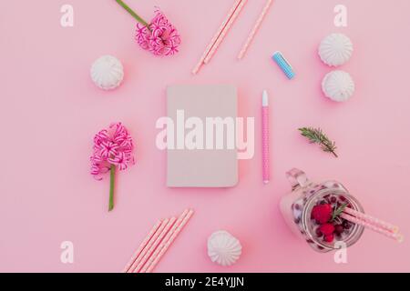 Leckere Smoothie mit Strohhalmen, Marshmallow, Tagebuch, Stift und rosa Blüten auf rosa. Flach liegend Stockfoto