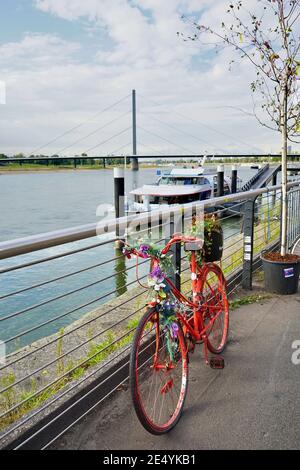 Ein rotes Deko-Fahrrad mit Blumen vor dem Restaurant "Kasematten" an der Rheinpromenade. Stockfoto