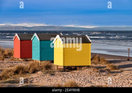 FINDHORN MORAY KÜSTE SCHOTTLAND DER STRAND MIT FARBIGEN CHALETS ODER HÜTTEN IM WINTER SCHNEEBEDECKTE BERGE DAHINTER Stockfoto