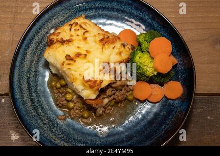 Ein köstlicher Teller mit Shepherds Pie mit Kartoffelpüree, Karotten und Broccoli auf einem hölzernen Küchentisch Stockfoto