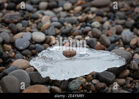 Ein winziger Felsen, der auf Eis liegt und von anderen umgeben ist Felsen Stockfoto