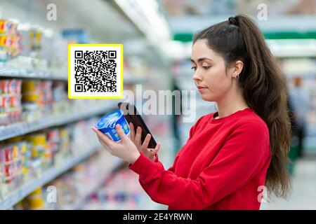 Einkaufen. Eine junge hübsche Frau scannt den qr-Code auf einem Produkt per Handy. QR-Code-Symbol über dem Produkt. Konzept der modernen Technologien und Shop Stockfoto