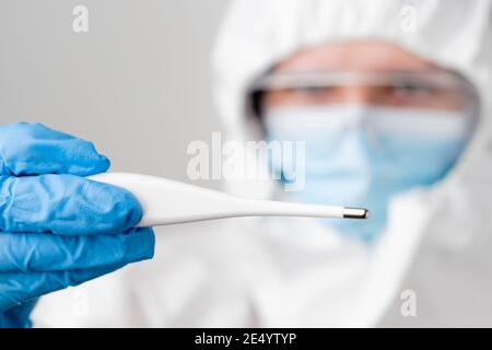 Digitales oder elektronisches Thermometer in der Hand des Arztes. Arzt oder Krankenschwester in schützenden PSA-Anzug, Gesichtsmaske, Sicherheits-Googles und Gummihandschuhe demonstriert Stockfoto