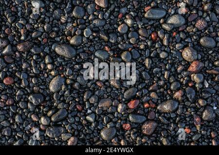 Schwarze nasse Seesteine am Strand, Blick von oben. Kann als Hintergrund verwendet werden. Stockfoto