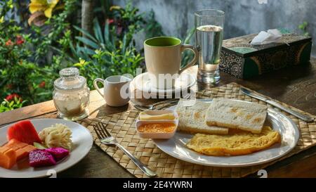 Traditionelles Touristenfrühstück auf Bali: Toast, Rührei, Kaffee und frisches Obst Stockfoto